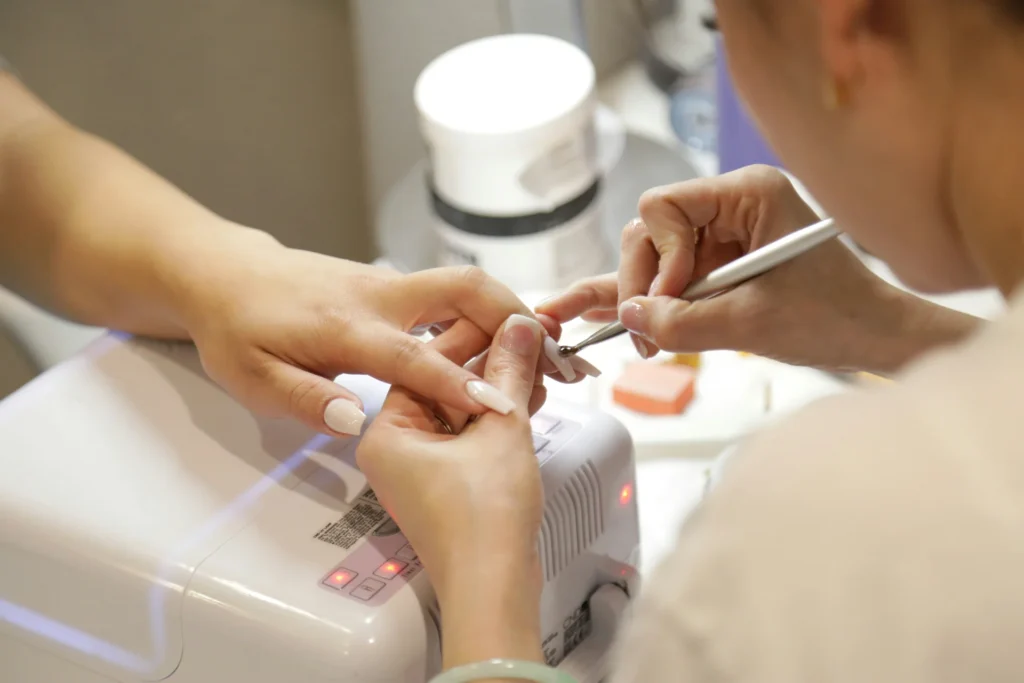 Kobieta w salonie kosmetycznym, której paznokcie są pielęgnowane przez manicurzystkę.