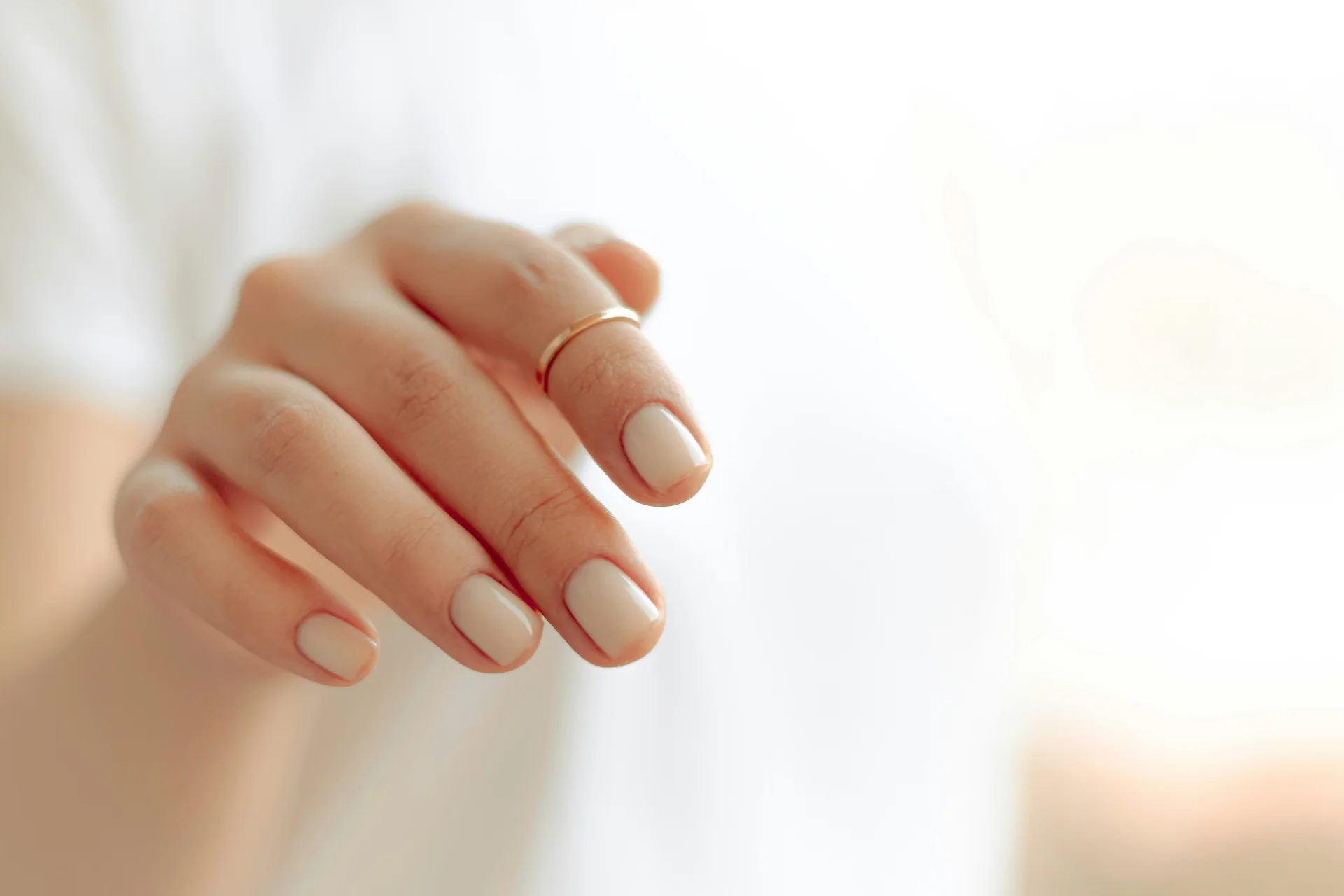 Zbliżenie na dłoń z eleganckim, białym manicure, prezentującym zadbane paznokcie.